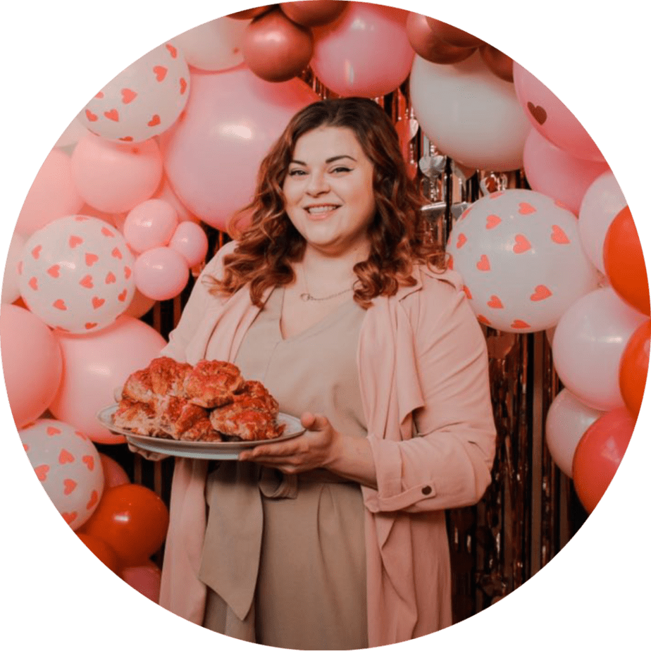 image of Autumn holding a plate of raspberry almond croissants. There is a pink, red, and white balloon arch behind her.
