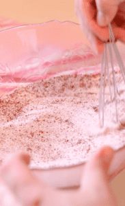 hand using a whisk to mix together dried peaches and sugar